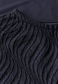 Tela azul oscura que presenta patrones ondulados texturizados con detalles fruncidos en la costura, resaltando la suavidad y profundidad del material.