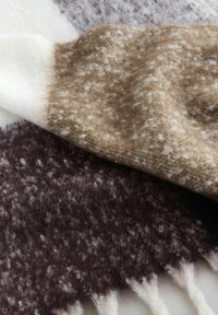 Měkká, chlupatá tkanina s hnědo-krémovým skvrnitým vzorem, přeložená přes tmavší, podobně texturovaný materiál s třásňovými okraji.