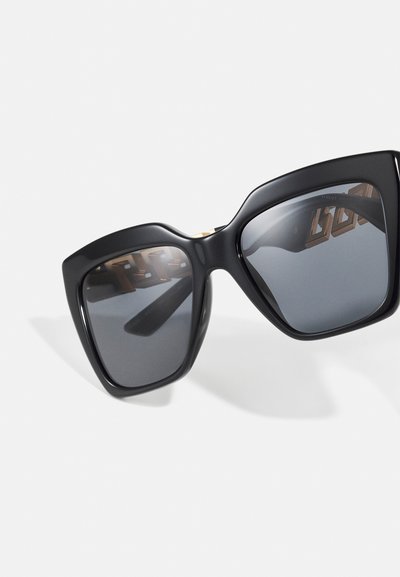 Óculos de sol oversized pretos com armação quadrada, lentes escuras e detalhes em dourado nas hastes. Textura suave com acabamento mate.