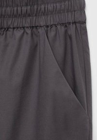 Elastische tailleband met een geplooide stiknaad op donkergrijze stof en een zijzak op de broek of short.