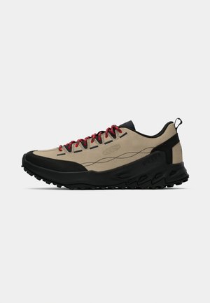 Beige and black outdoor sneaker with textured sole and red laces, low-cut design, and fabric pull tab at heel.