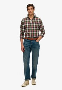 Heren geruit overhemd met groen, rood en witte ruiten, met een button-downkraag, gecombineerd met een blauwe spijkerbroek en beige sneakers.