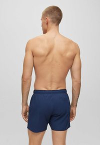 Marineblaue Schwimmshorts mit einem elastischen Bund und einer Gesäßtasche, hergestellt aus leichtem Stoff. Das Design ist einfach und funktional.
