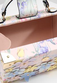 Torebka z kwiatowym wzorem w pastelowych kolorach, z gładką skórzopodobną teksturą. Wnętrze ma jednolitą różową podszewkę. Ozdobne kwiatowe akcenty z przodu.