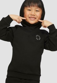 Felpa nera con tasca frontale e polsini a coste. Presenta un logo rotondo sul petto. Bambino sorridente che indica le guance.