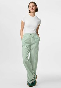 T-shirt blanc ajusté à manches courtes associé à un pantalon ample à rayures vertes avec une taille élastique et des poches latérales, porté avec des baskets vertes.