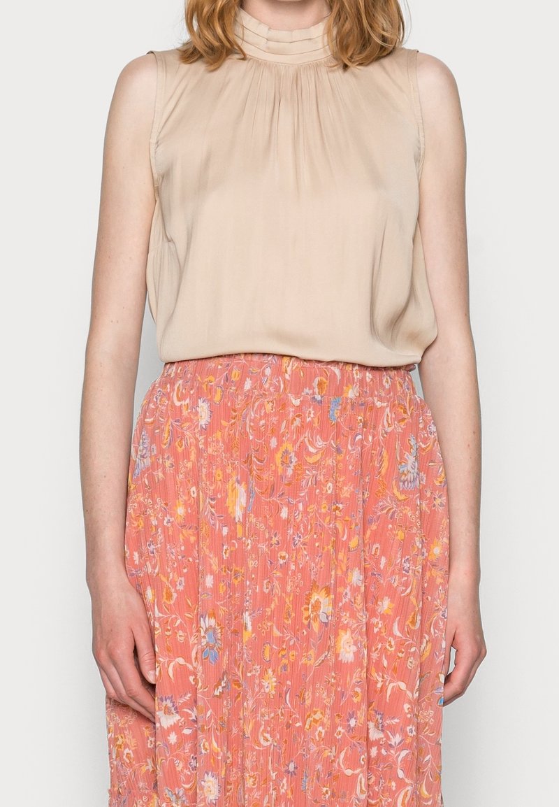 Beige ærmeløs top med plisseret design, parret med en lang, blomsterprydet lyserød nederdel med vertikale striber og pastelfarver.