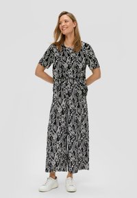 Schwarz-weiß gemusterter Jumpsuit mit kurzen Ärmeln, geraffter Taille und weitem Bein, kombiniert mit weißen Sneakern.