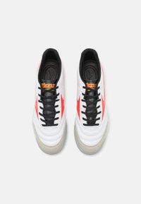 Zapatillas deportivas blancas y rojas con parte superior de cuero suave, cordones negros y suela de goma gris. Presenta logotipo y cuello acolchado.