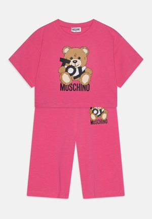 Šviesiai rožinė medvilninė dvejopa apranga, kurią sudaro trumpomis rankovėmis viršus su meškiuko grafika ir atitinkantys šortai, abiem su "Moschino" prekių ženklu.