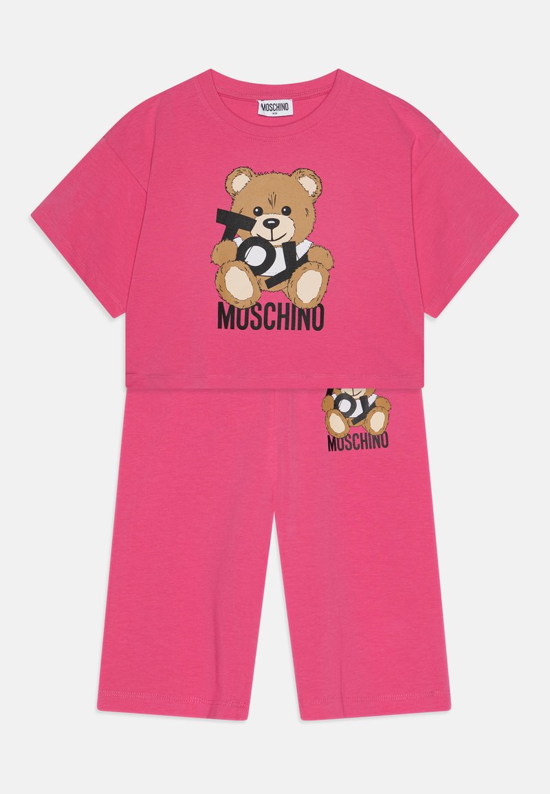 Gaiši rozā kokvilnas divdaļīgais komplekts, kurā ietilpst īsām piedurknēm tops ar teddy bear grafiku un atbilstošas šortus, abi ar "Moschino" zīmolu.