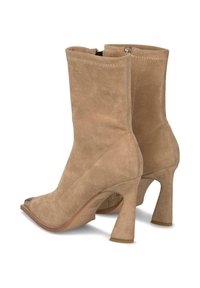 Botines de ante beige con puntera puntiaguda, que cuentan con un cierre de cremallera y un tacón grueso. Textura suave y diseño minimalista.