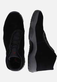 Para czarnych sneakersów za kostkę z szarymi podeszwami, z czerwonym logo na języku, widoczna z perspektywy góry i boku na białym tle.