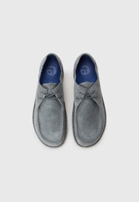 Grey suede shoes with a rounded toe, featuring two lace-up accents and a blue insole. The stitching is contrasting and visible along the edge.