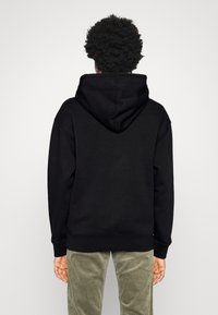 Sudadera negra con una capucha grande, puños y dobladillo acanalados, hecha de un material suave y texturizado, con un corte relajado y sin logotipos visibles.