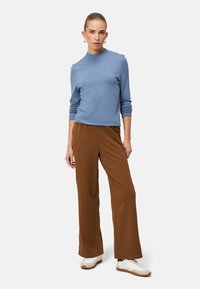 Light blue, long-sleeve crew neck sweater paired with high-waisted, wide-leg brown trousers and white athletic shoes. Smooth fabric, relaxed fit.
