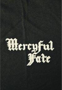 Bílé gotické písmo zní "Mercyful Fate" na černém textilním pozadí.