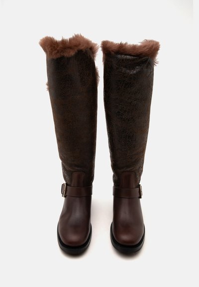 Bottes hautes marron foncé avec doublure en fourrure en haut et sangles à boucle autour de la cheville.