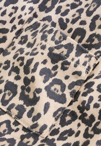 Leoprint-Stoff mit dunkelgrauen Flecken auf hellbeigem Hintergrund, mit sichtbaren Textur- und Nahtdetails.