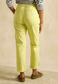 Heledad kollased puuvillased püksid, millel on tikitud lillemustrid, pakkudes mugavat istuvust, elastset vöökohta ja üleskeeratud varrukaid. Pruunid sussid.