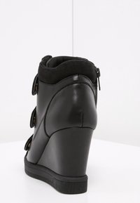 Svart kilklack stövlett med en slät läderutsida och krage i mocka. Har tre remmar med metallknappar och en sidodragkedja.