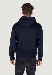 Felpa con cappuccio blu navy dal taglio rilassato, dotata di tasca a marsupio e polsini a coste. Il tessuto sembra morbido con una superficie liscia.