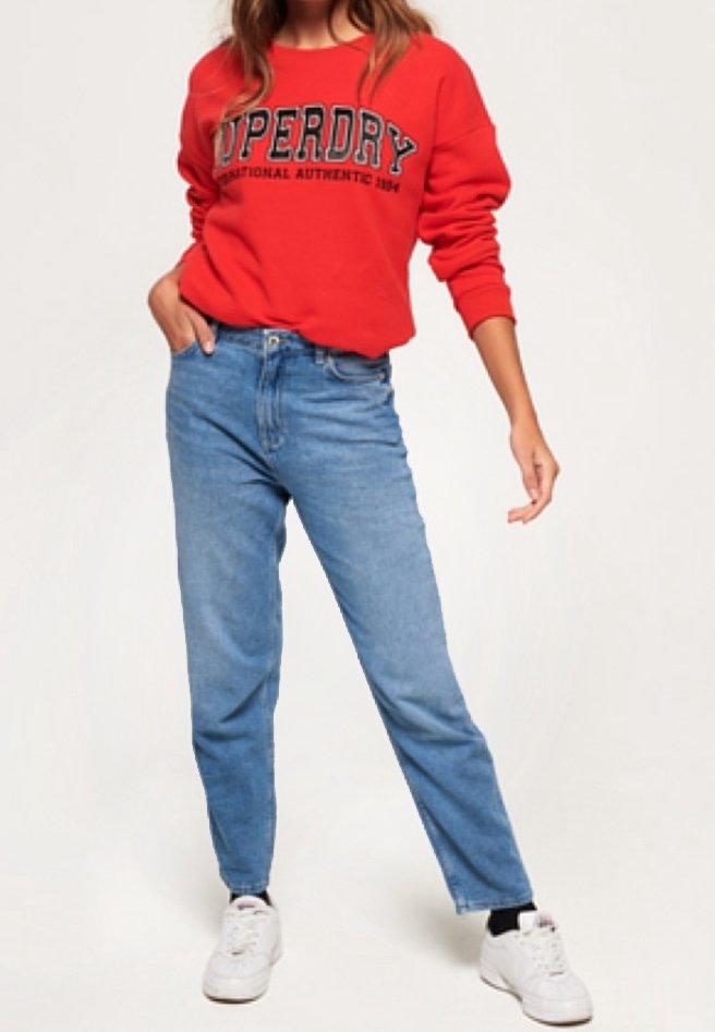 Sudadera roja con el texto "Superdry", acompañada de jeans rectos de color azul claro y zapatillas blancas. La tela parece suave, con un ajuste casual.