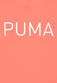 Camiseta de color coral con cuello redondo que muestra la palabra "PUMA" en letras blancas en negrita en la parte frontal, con textura suave.