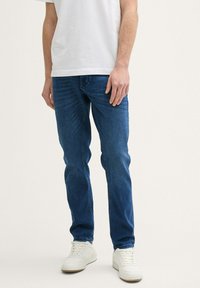 Vaqueros de mezclilla azul con un corte recto, que presentan un diseño clásico de cinco bolsillos y una ligera textura deslavada, combinados con zapatillas blancas.