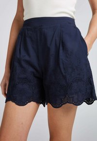 Shorts bleu marine avec broderies florales et ourlet en dentelle festonnée. Design plissé, poches latérales, fabriqués dans un tissu léger.