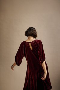 Bordeaux Samtkleid mit puffierten Ärmeln, Schlüsselrücken und fließender Silhouette; die glatte Textur und die satte Farbe werten das Design auf.