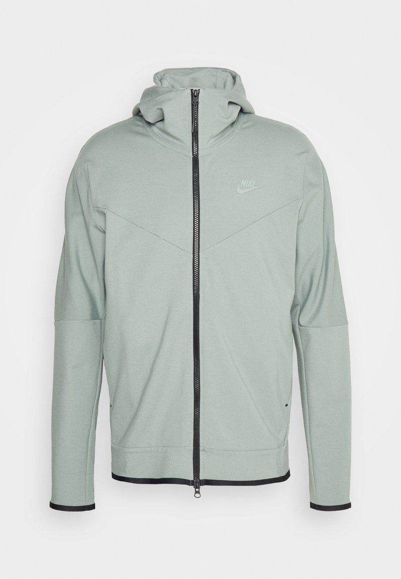 Haut de hoodie Nike vert clair avec un col montant, fermeture à glissière frontale, design en chevrons sur la poitrine, et bord noir au bas et aux manches.