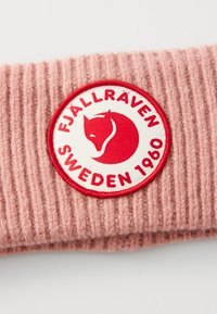 Roze gebreide stof met een ronde witte en rode patch met een voskop en de tekst "Fjällräven Sweden 1960."