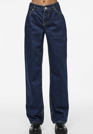 Dark blue high-waisted straight-leg jeans worn with black shoes, shown from waist to feet against a white background.