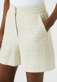 Cremfarbene Shorts mit glatter Oberfläche, ausgestattet mit Seitentaschen und einem geraden Saum. Maßgeschneiderter Bund für eine strukturierte Passform.