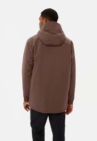 Giacca cappuccio marrone con vestibilità rilassata, polsini elasticizzati e una texture liscia, resistente all'acqua. Presenta un design semplice senza decorazioni.