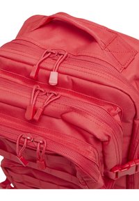 Punainen kangasreppu, jossa on useita vetoketjullisia osastoja, vahvistetut saumat ja säädettävät olkahihnat turvallista kantamista varten.