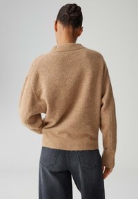 Brauner Strickpullover mit lockerem Schnitt, geripptem Saum und langen Ärmeln, kombiniert mit hoch taillierten dunkelgrauen Jeans. Strukturierter Stoff.