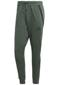 Zelené sportovní tepláky s pružným pasem na šňůrku, zúženým střihem, bočními zipovými kapsami a černými logovými akcenty. Měkká, texturovaná látka.