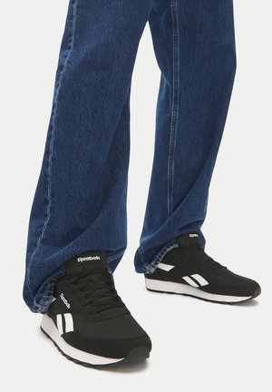 Reeboki mustad tossud valgete detailidega, paeltega kinnitatavad, polsterdatud kaeluse ja tekstuurse kummipõhjaga. Kandmisel siniste teksadega.