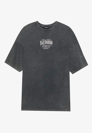 T-shirt oversized gris en tissu doux. Présente un col rond et des manches courtes. Le graphique à l'avant affiche "SAN DIEGO Californie" en blanc.