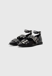 Black pointed flat shoes with multiple silver buckles and grommeted straps, including ankle straps, on a white background.