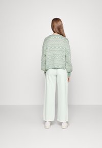 Mintgrüner Strickpullover mit geometrischen Mustern, kombiniert mit weiten mintfarbenen Hosen und hellen Sneakern. Rückansicht des Outfits.