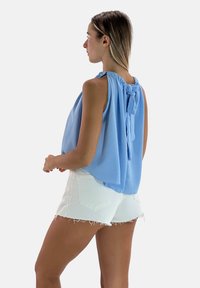 Blusa senza maniche azzurro chiaro con scollo arricciato e dettaglio a fiocco sul retro, abbinata a pantaloni corti bianchi con orlo sfrangiato.