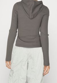 Haut à manches longues côtelé gris foncé avec capuche, porté avec un pantalon cargo clair présentant des poches latérales et une texture douce.