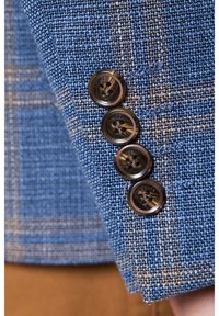 Niebieska tkanina o fakturze z tkanym wzorem; zawiera cztery ciemne guziki o gładkim wykończeniu na mankiecie.
