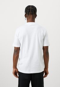 Hvit t-skjorte med korte ermer og rund hals, laget av bomull, med en jevn tekstur og avslappet passform, vist fra ryggen.