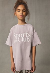 Lilac oversized t-shirt with "Sports Club 1982" graphic in white. Short sleeves and a slightly textured fabric, paired with leopard print leggings.