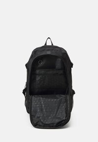 Sac à dos en tissu noir avec une ouverture zippée, des poches intérieures et une poche latérale en mailles. Comprend une boucle pour attacher un porte-clés.