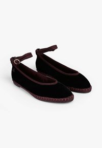 Bailarinas de terciopelo negro con una correa de tobillo burdeos, detalles de costura y punta redondeada. Textura suave y diseño minimalista.